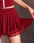 Detail shot of Pom Pêche wine red Waltz skirt showing double-layer pleated hem with sheer mesh underlayer and Pom Pêche metal logo tag – soft LYCRA® blend with anti-static finish
