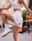 Model jumping in Pom Pêche white high-slit tennis shorts on Paris street, showcasing freedom of movement and side slit design with tricolor stripe