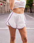 Pom Pêche High-Slit Contrast Active Shorts in white – front view showing relaxed fit, drawstring waistband and contrast stripe detailing, worn on Paris street.
