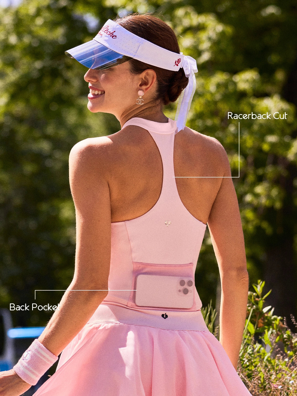 Back view of Pom Pêche blush pink Zip-Neck Halter Tank with feature callouts – open Racerback Cut for unrestricted movement and Back Pocket holding phone annotated, Pom Pêche logo detail, Paris garden background