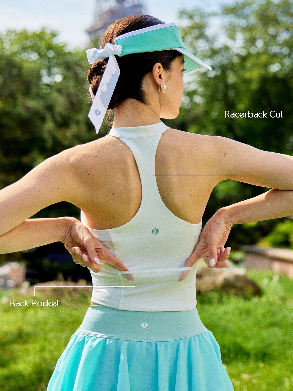 Back view of Pom Pêche white Zip-Neck Halter Tank with feature callouts – open racerback cut for unrestricted movement and back zip pocket annotated, Pom Pêche logo detail, Paris Eiffel Tower garden