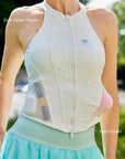 Close-up of Pom Pêche white Zip-Neck Halter Tank with feature callouts – dual-zipper design with Pom Pêche logo and side mesh pockets shown with lipstick inserted, styled with mint skirt