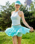 Full body view of Pom Pêche Zip-Neck Halter Racerback Tank in white – high halter neckline, front zip closure and fitted silhouette, styled with mint tiered ruffle skirt and Pom Pêche visor in Paris garden