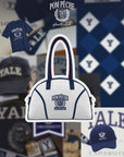 Cream dome tennis bag with contrast handles and Pom Pêche logo, styled on a tennis court.