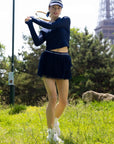 Spin Layered Mesh Pleated Tennis Skirt Navy on tennis court, showcasing dynamic movement, lightweight pleated mesh, built-in shorts, and stylish athletic performance